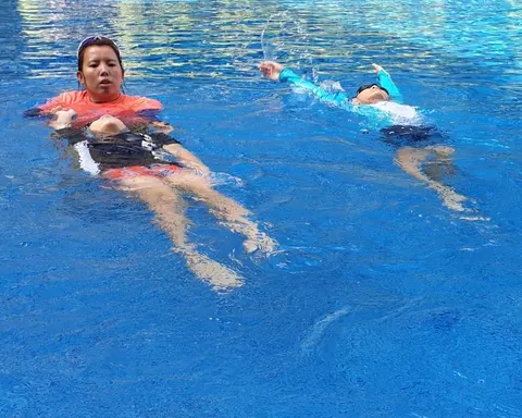 Coach Jina demonstrating a back float beside a boy swimming backstroke