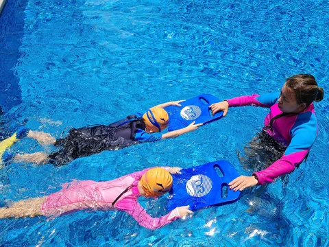 Coach Jina correcting the kick of two young swimmers on kickboards