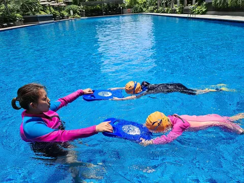 Coach Jina guiding two children through a kickboard kick drill