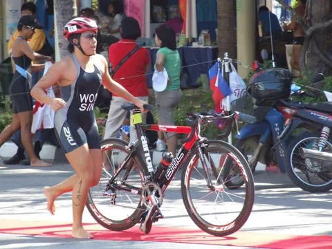 Jina wheeling her bike through transition in a Singapore “WOO SIN” race suit at the 2007 SEA Games triathlon