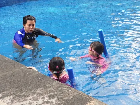 Coach Jina instructing two young girls holding noodles in a condo pool