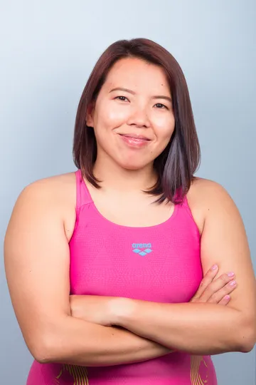 Coach Jina Woo in a pink swimsuit, arms crossed, smiling