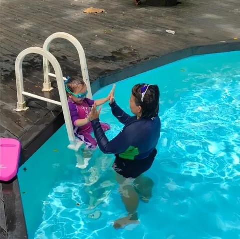 Coach Jina giving a high-five to a toddler on the pool ladder